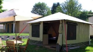 A camping site with a tent, a table with chairs, and a small building in the background.