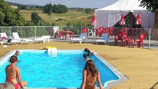 A pool area with a wooden deck, lounge chairs, and a tent in the background.