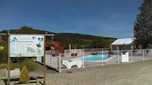 A pool area with a fenced deck, a signboard with information, and a view of the surrounding landscape.