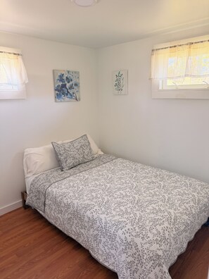 A bedroom with a single bed, white walls, and two windows with sheer curtains. - Escape to your private Lake Huron retreat with 6 fully equipped cottages, 13 bedrooms, and 6 bathrooms, perfect for family reunions, weddings, retreats, and group getaways. (Iosco County)