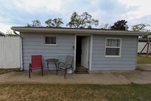 A small single-story house with a front door, two windows, and a small porch area with a table and two chairs. - Escape to your private Lake Huron retreat with 6 fully equipped cottages, 13 bedrooms, and 6 bathrooms, perfect for family reunions, weddings, retreats, and group getaways. (Iosco County)