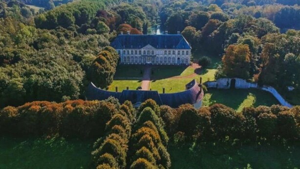 Luchtbeeld van een groot landgoed met een centraal gebouw, omringd door weelderig groen en een gracht.