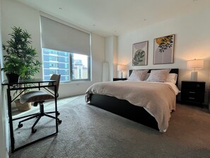 A bedroom with a bed, a desk with a chair, a potted plant, and artwork on the walls. - Classy 1-bedroom condo in Little Italy, Downtown San Diego, with AC, gym, valet (San Diego)