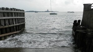 Vista al agua con muelle de madera, aguas tranquilas y barcos a lo lejos.