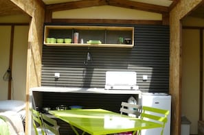 A compact kitchen with a table and chairs, a small shelf above the counter, and a refrigerator. - ZEcamping 3* piscine chauffée hammam locatif BBQ 17m2 4 pers (Louvie-Juzon)