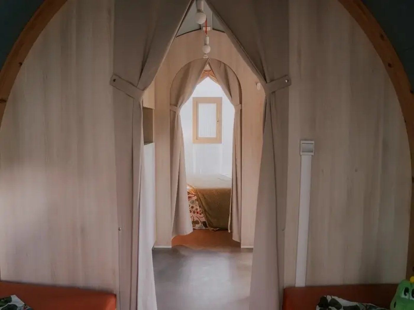 Ein gewölbter Gang führt zu einem Schlafzimmer mit Bett und Fenster.