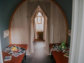 Une pièce dotée d’une haute porte en arc donnant sur une chambre à coucher. On y trouve deux lits avec une literie à motifs floraux et un jouet vert sur l’un des lits.
