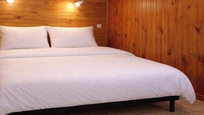 A wooden-paneled room with a bed, two bedside lamps, and a carpeted floor.