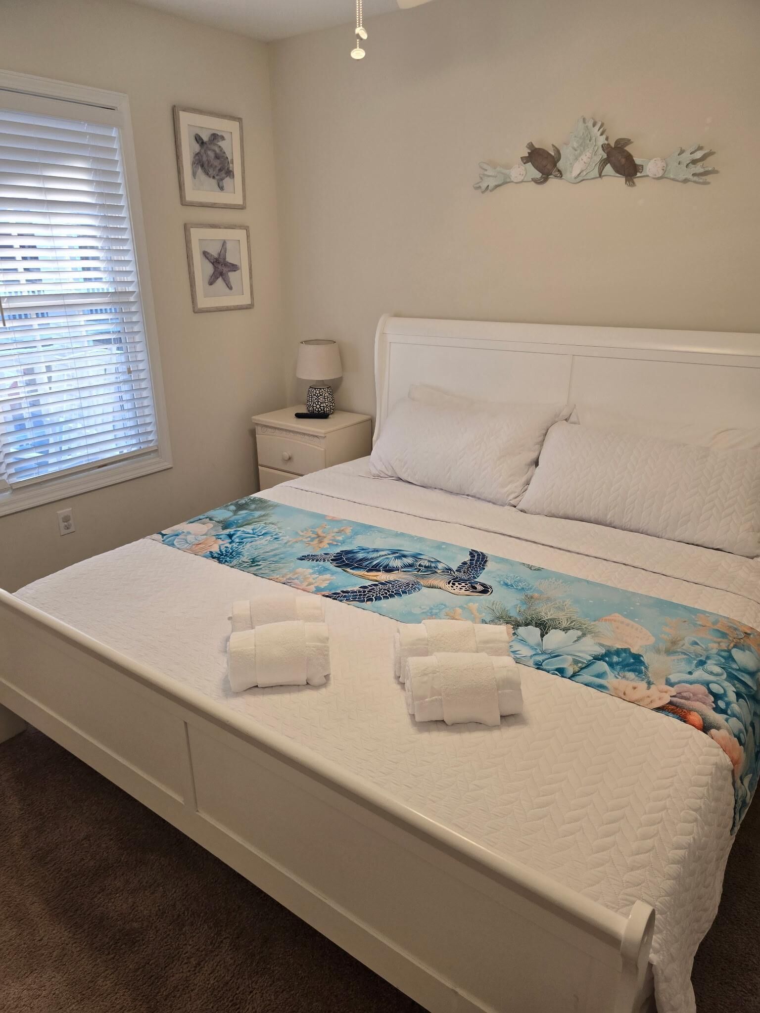 A bedroom with a bed, a nightstand, a lamp, and wall decorations including starfish and birds.