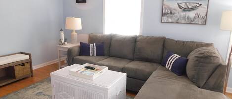 A living room with a grey sofa, a white coffee table, a lamp, and a painting on the wall.