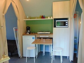 A compact kitchenette with a microwave, a small fridge, and a coffee maker. There are two white stools and a table with four glasses. - ZEcamping 3* animé piscine couverte pet friendly locatif 16m2 4 pers (Avrillé)