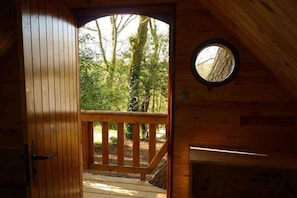 Una cabaña de madera con terraza, un ventanal circular y una puerta que da a un espacio al aire libre.