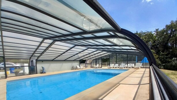 Ein Schwimmbecken mit Glaskuppel, umgeben von Liegestühlen und einer überdachten Terrasse.