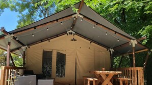 Ein zeltähnlicher Außenbereich mit einer Holzterrasse, Sitzgelegenheiten und einem Tisch.