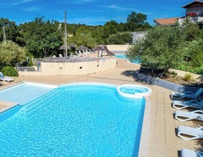 Une piscine avec des chaises longues, un espace ombragé et un bâtiment en arrière-plan.