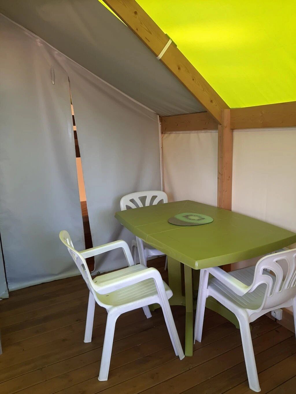 Een klein eethoekje met een tafel en vier stoelen, een houten plafond en een wit gordijn.