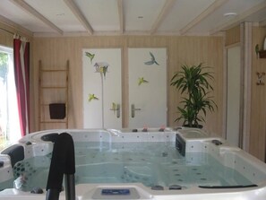 Ett spa-rum med ett bubbelbad, väggar beklädda med träpaneler, en stege och dekorativa fågelmotiv.