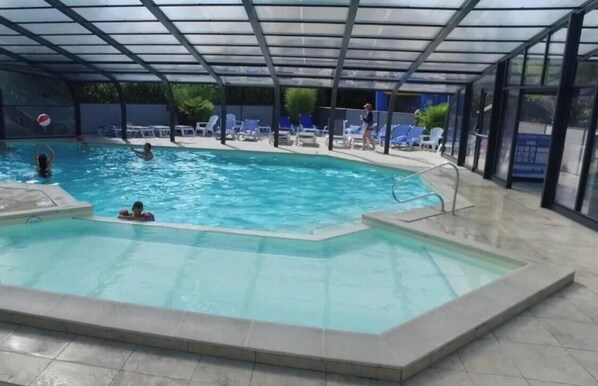 En inomhuspool med klart vatten, omgiven av solstolar och ett överbyggt område.
