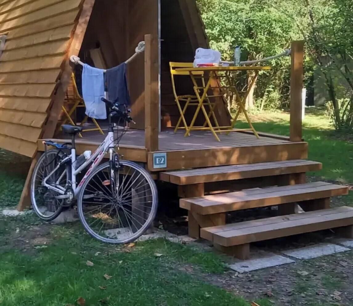 A wooden tent with a bicycle parked outside, wooden steps leading to a platform, and a table with chairs.