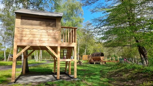 A wooden cabin with a balcony, a barrel, and a forested background.