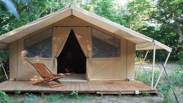 Uma tenda com deck de madeira, uma cadeira e uma janela.