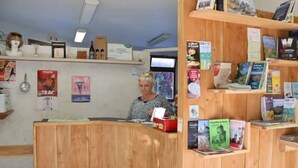 Um balcão de recepção com bancada de madeira, uma televisão e diversos folhetos e livros de viagens em prateleiras.
