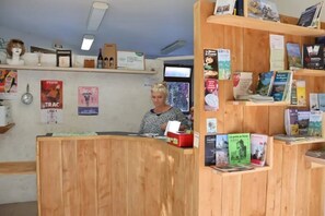 Un comptoir d’accueil avec un plan de travail en bois, un téléviseur, ainsi que divers dépliants et livres sur le thème du voyage, disposés sur des étagères.