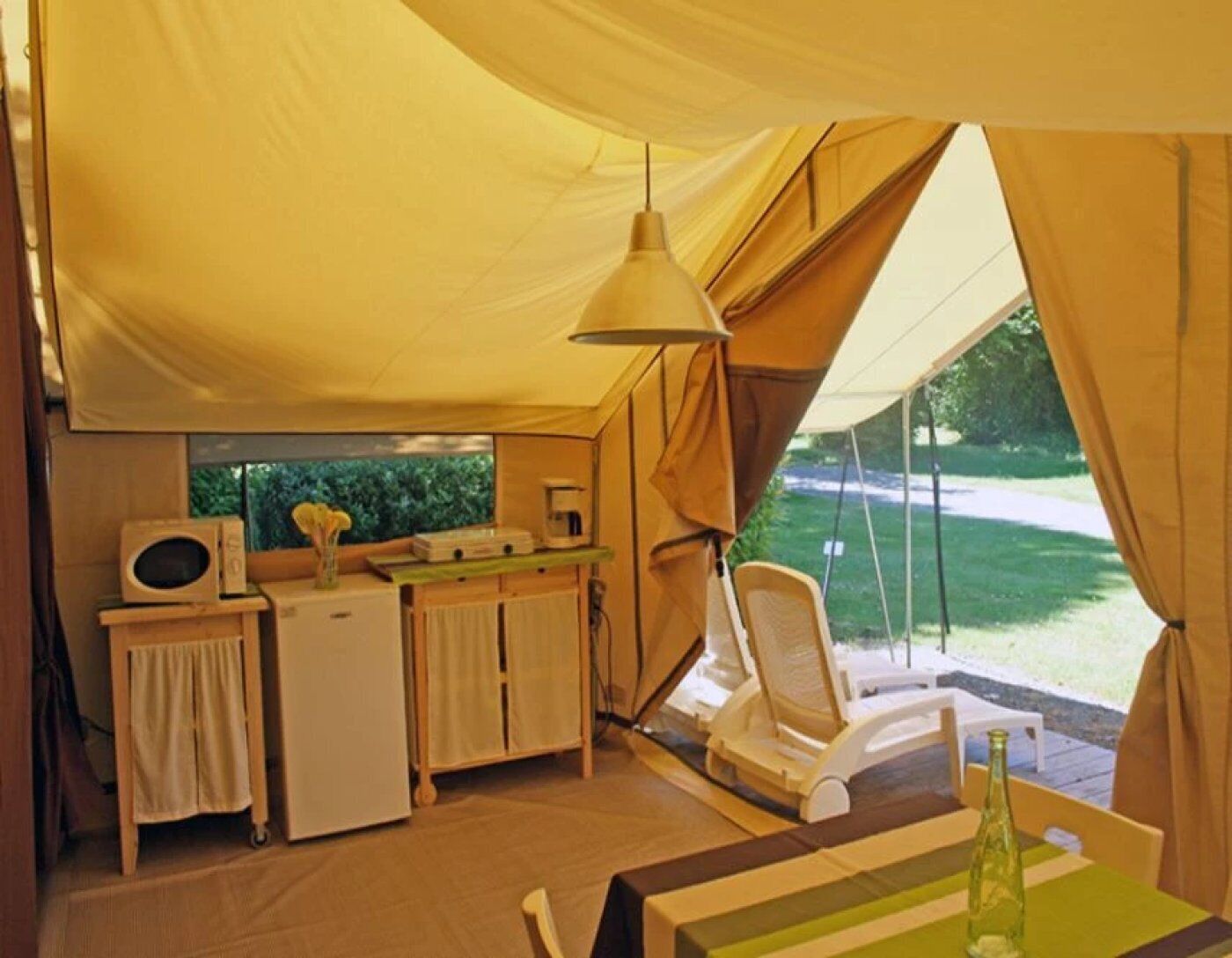 A tent with a kitchenette, a table with chairs, and a view of a green landscape.