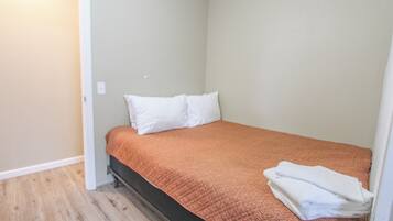 A small, single-bed room with a wooden floor, white walls, and a brown bedspread.
