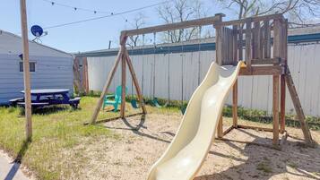A backyard with a wooden swing set, a slide, a picnic table, and a satellite dish.