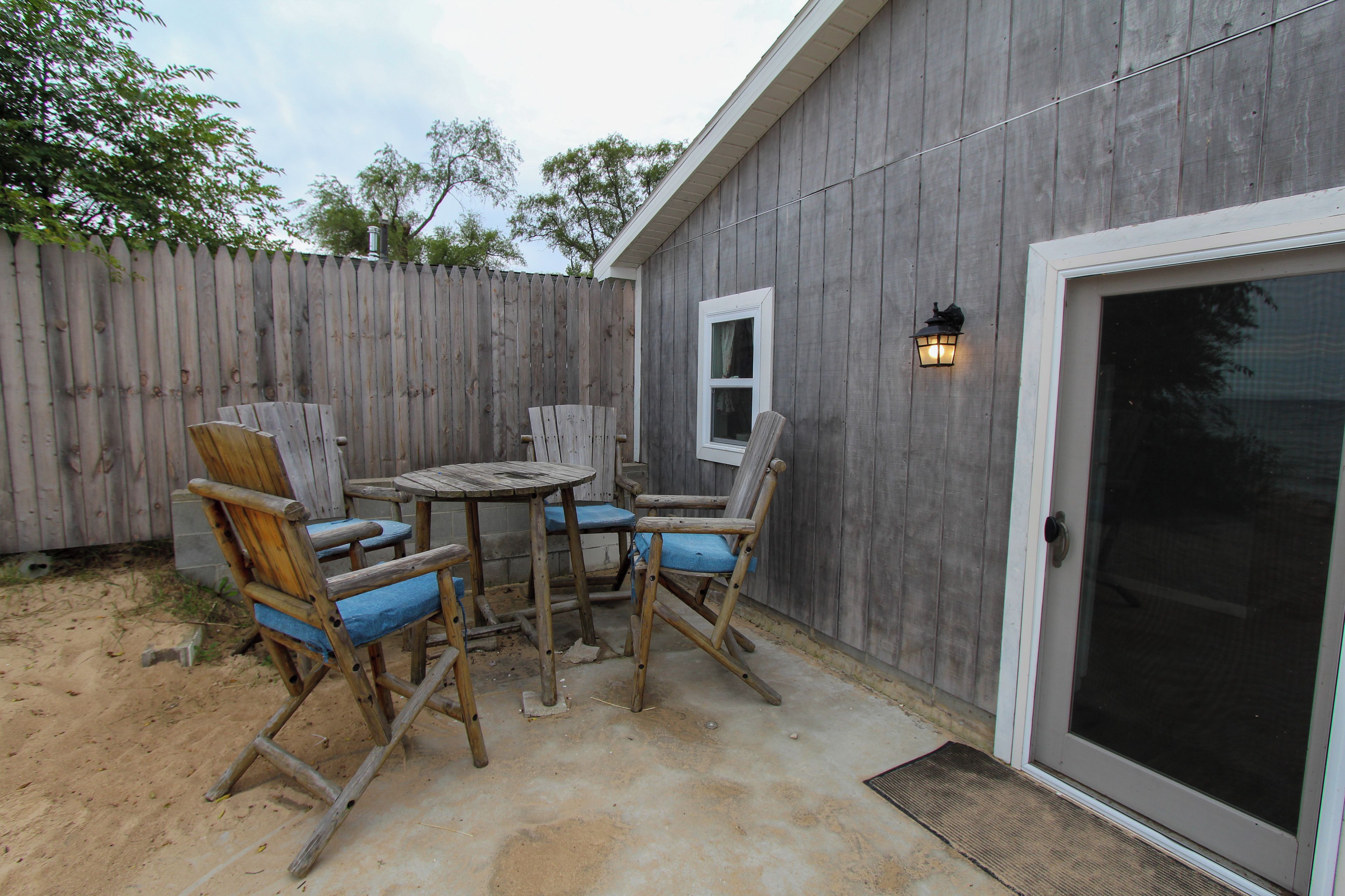 Un patio exterior con una mesa y sillas de madera, una ventana y una puerta con mosquitero.
