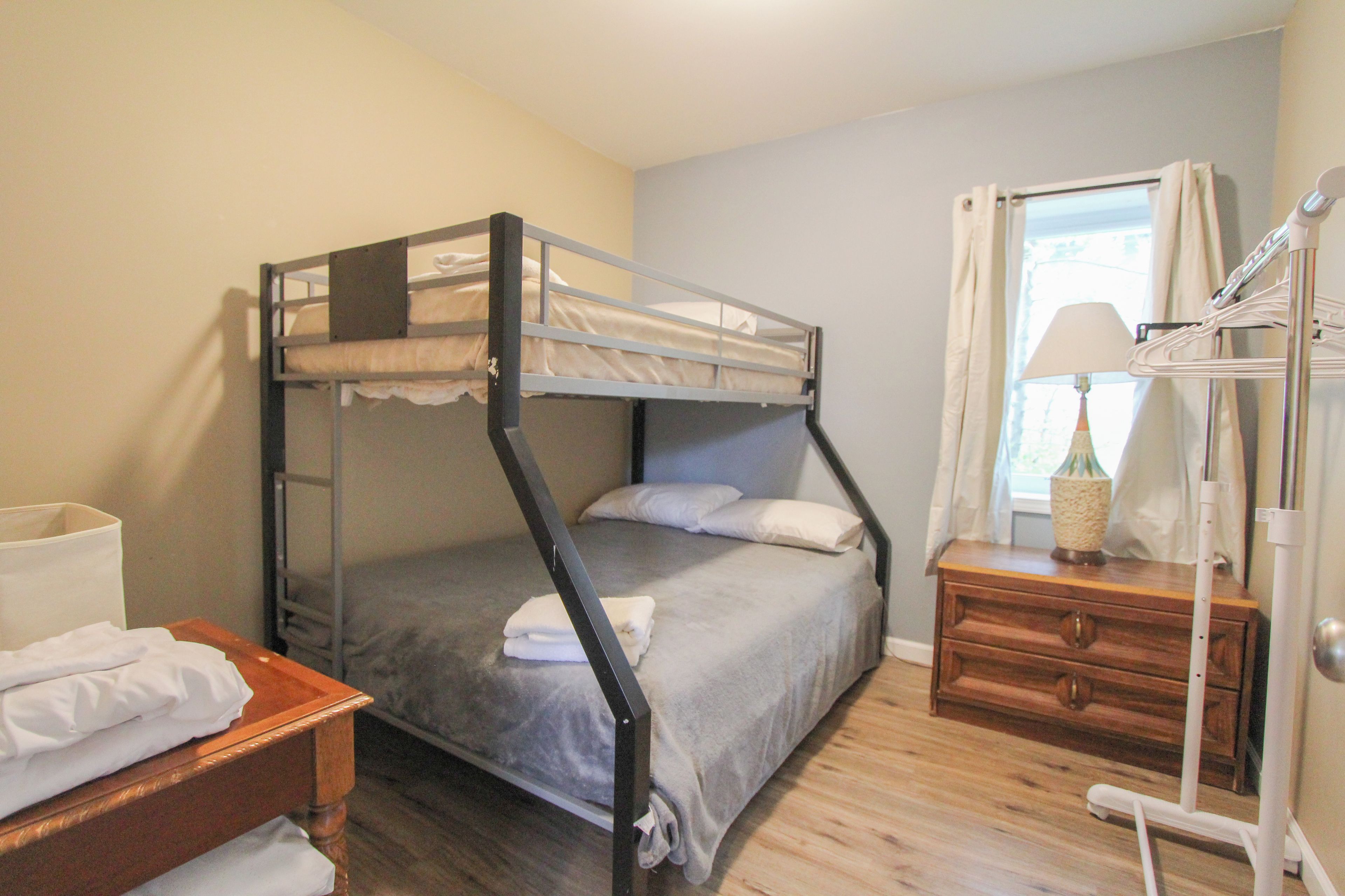 A bunk bed with a wooden dresser and a lamp beside a window.