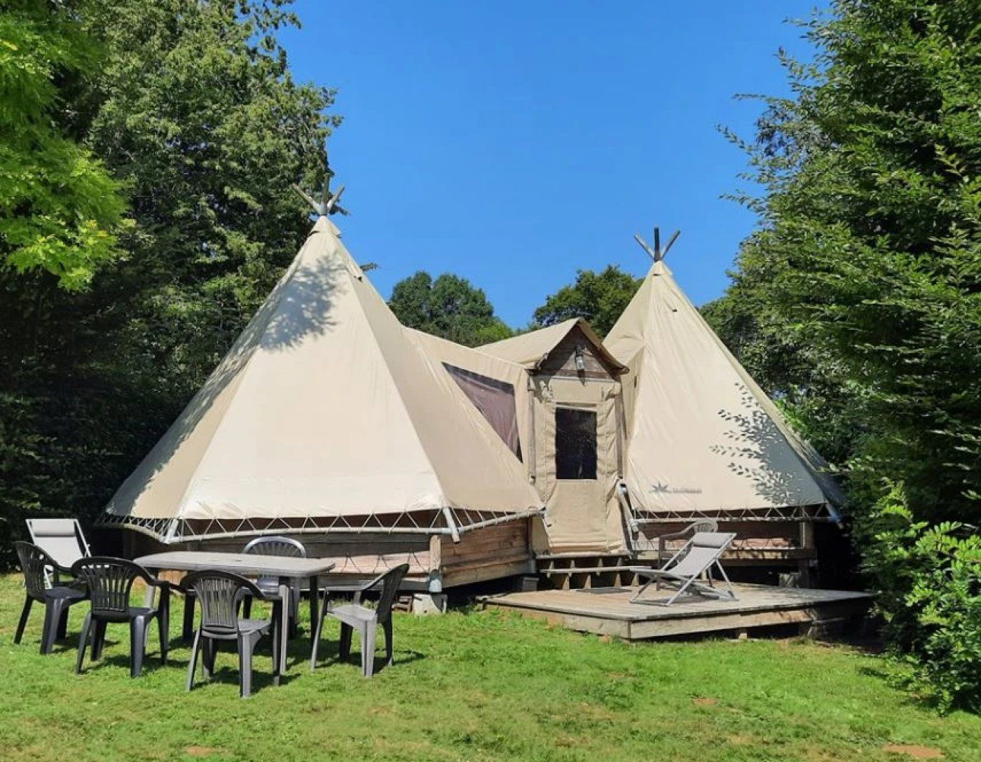 A camping site with two conical tents, a wooden deck, and outdoor furniture.