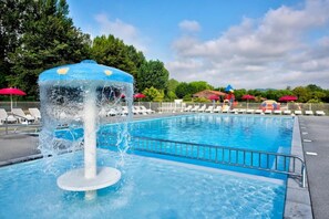 Ein Schwimmbecken mit Springbrunnen, umgeben von Liegestühlen und Sonnenschirmen.