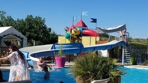 Une piscine avec un toboggan et une structure de jeux en arrière-plan.