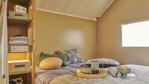 Une chambre confortable avec un lit, des oreillers, une table de chevet sur laquelle se trouvent une tasse et un mug, et une fenêtre.