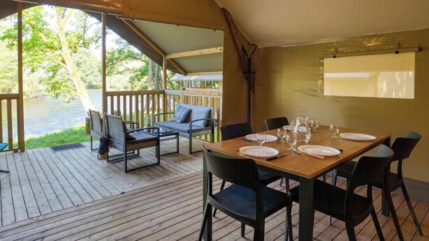 Un espace extérieur abrité, aménagé pour les repas, avec une table en bois pour quatre personnes, entourée de chaises, et offrant une vue sur une rivière.
