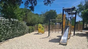 Zona de juegos arenosa con un tobogán y estructuras para escalar.