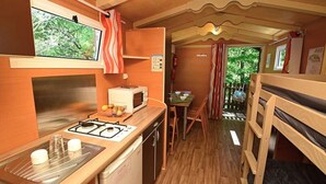Een compacte keuken met een gasfornuis, magnetron en spoelbak. Er is een eethoek met een tafel en stoelen, en uitzicht op het buitengebied door een raam.