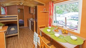 Een compacte kamer met stapelbedden, een kitchenette, een eethoek met een tafel voor twee personen, en een raam met uitzicht op de omgeving.