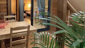 A wooden cabin with a dining area, a bed, and a sliding glass door leading to a bedroom.