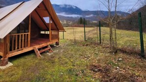 A wooden cabin with a sloped roof, a porch, and a fenced yard.