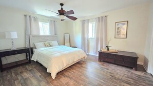 Un dormitorio con cama, mesita de noche, cómoda, ventilador de techo y un cuadro en la pared.