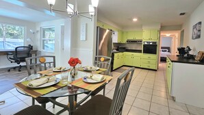 Una cocina moderna con armarios verdes, un refrigerador de acero inoxidable y un comedor con mesa y sillas de vidrio.