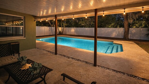 Un espacio al aire libre techado con piscina, asientos y luces colgantes.