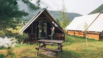 A cabin with a large sliding door, a picnic table, and a view of a lake and mountains.