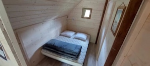 A small, wooden room with a bed, a window, and a mirror.