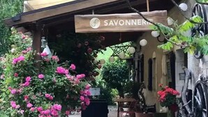 A covered outdoor seating area with a sign reading 'SAVONNERIE,' surrounded by lush greenery and flowering plants.