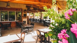 An outdoor cafe with wooden tables and chairs, large windows, and hanging plants. - ZEcamping 3* piscine pet friendly chalet 3 pers (Saint-Remèze)