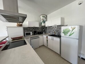 Eine moderne Küche mit weißen Schränken, einer Mikrowelle, einem Spülbecken und einem Kühlschrank mit Pflanzenmuster.